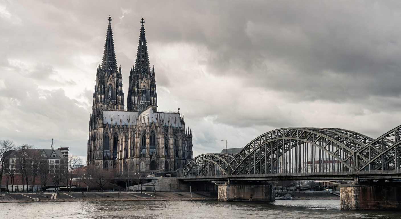 Cologne Cathedral majestic Gothic twin spires rising into cloudy sky with Rhine River and Hohenzollern Bridge visible